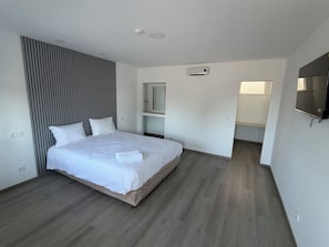 A modern bedroom with a large bed, a built-in wardrobe, a television, and a bathroom visible through an open door. - Alojamento Local Cova Da Serpe (Figueira da Foz)