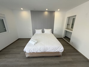 Habitación de hotel moderna con una cama grande, piso de madera, cabecera a rayas y un banco integrado con espacio de almacenamiento.