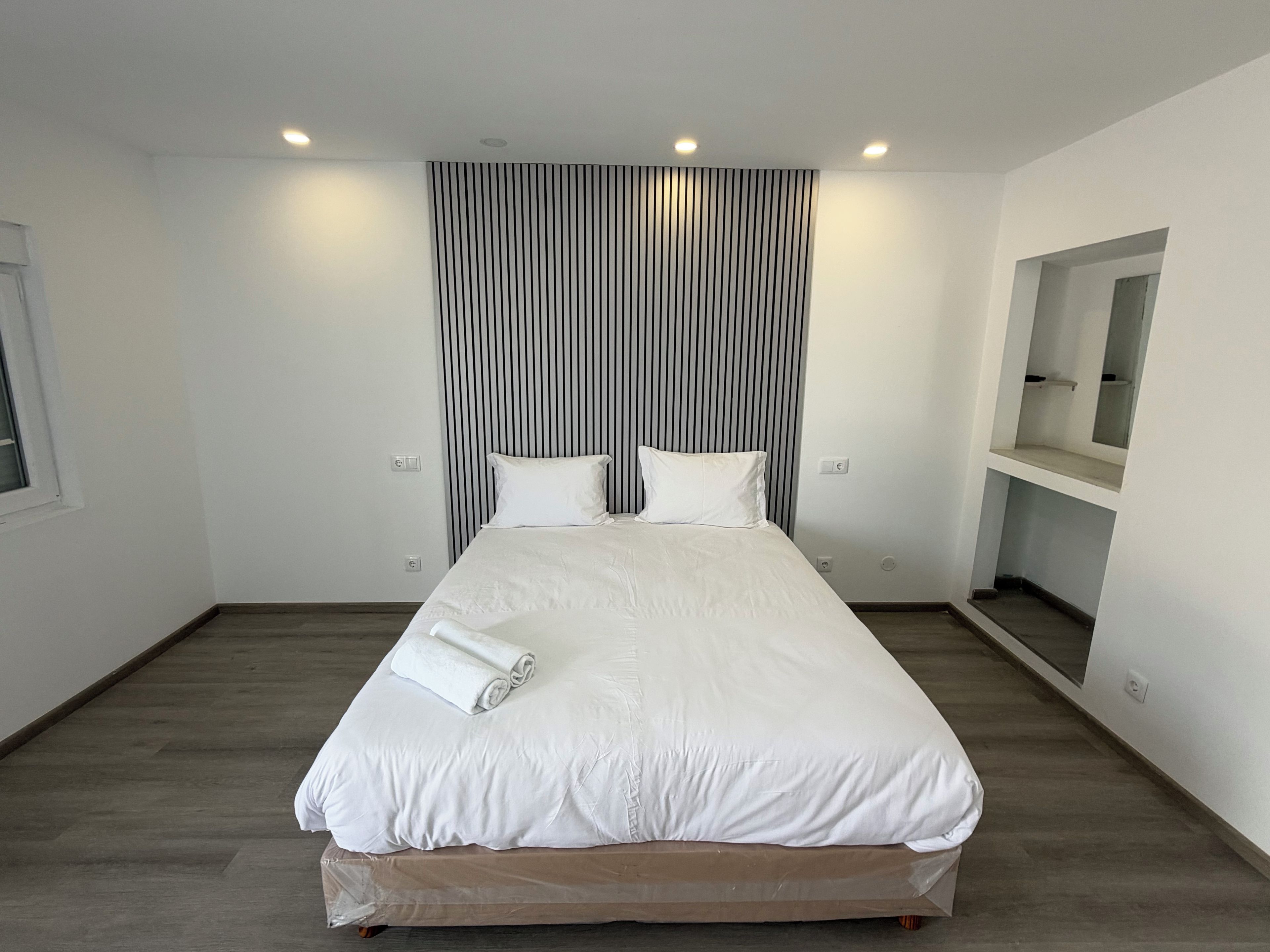 Habitación de hotel con una cama grande, suelo de madera, cortina a rayas y un espejo pequeño en la pared.