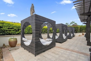 Móveis de vime para área externa, com detalhes recortados em círculo, um vaso grande e uma estrutura de pérgola.