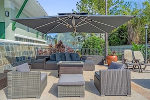 An outdoor seating area with a large umbrella, wicker furniture, and a potted plant. - Family Getaway Near Disney With Pool and Games (Orlando)