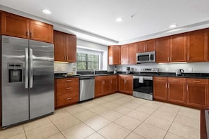 A modern kitchen with stainless steel appliances, wooden cabinets, and a large window. - Family Getaway Near Disney With Pool and Games (Orlando)