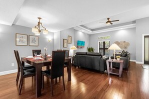 A dining area with a wooden table and chairs, a sofa, and a small side table with a lamp. - Family Getaway Near Disney With Pool and Games (Orlando)