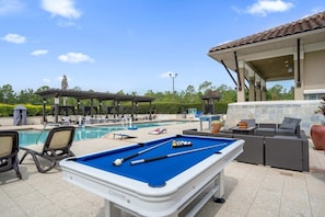 A pool area with a blue pool table, lounge chairs, and a covered seating area. - Family Getaway Near Disney With Pool and Games (Orlando)