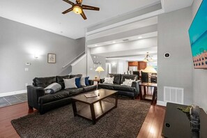 A modern living room with a dark brown coffee table, two black leather sofas, a dark rug, and a ceiling fan. - Family Getaway Near Disney With Pool and Games (Orlando)