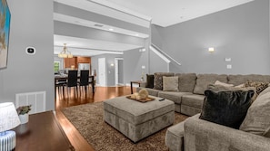 A modern living room with a sectional sofa, a coffee table, and a rug. There is a dining area visible in the background. - Group Disney Stay With Pool Spa Game Amenities (Orlando)