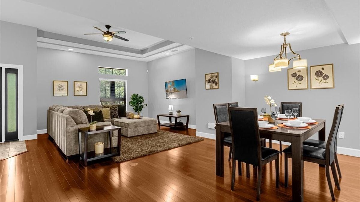 Uma sala de estar moderna com área de jantar, apresentando um conjunto de sofá, mesa de centro, mesa de jantar com cadeiras e ventilador de teto.