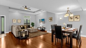 A modern living room with a dining area, featuring a sofa set, a coffee table, a dining table with chairs, and a ceiling fan. - Group Disney Stay With Pool Spa Game Amenities (Orlando)