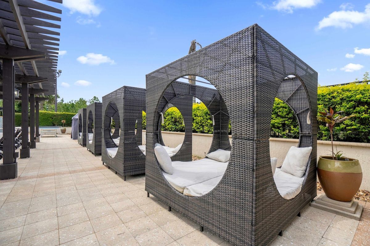Outdoor wicker seating areas with cushions, a pergola structure, and a large planter.