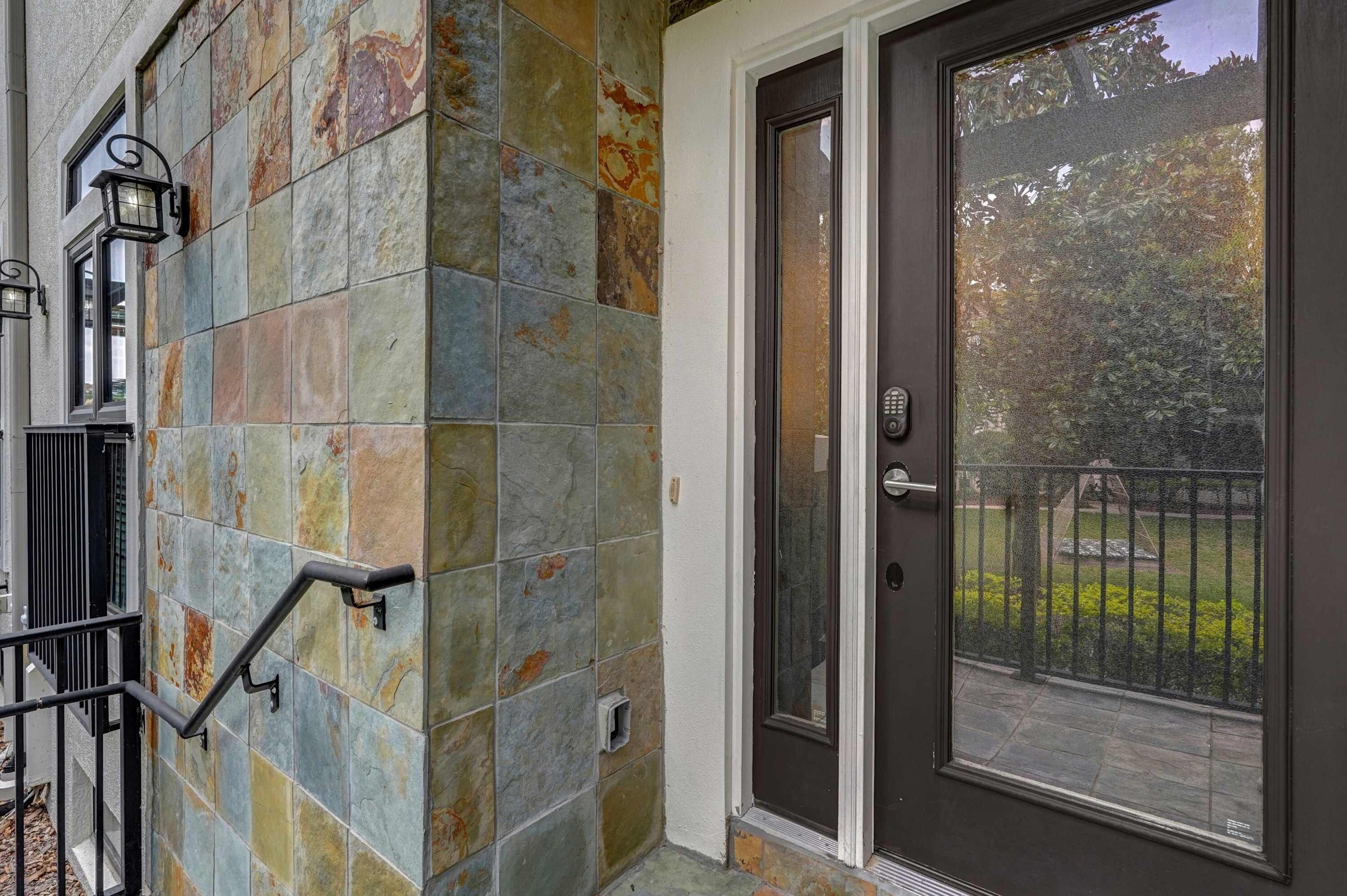 A building exterior with a stone facade, a door with a glass panel, and a metal handrail.