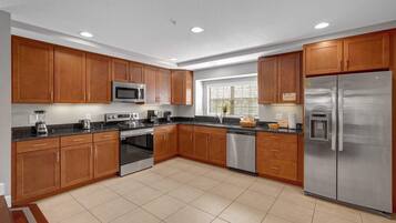 A modern kitchen with wooden cabinets, stainless steel appliances, and a tiled floor.