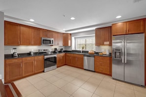Una cocina moderna con armarios de madera, electrodomésticos de acero inoxidable y suelo de baldosas.