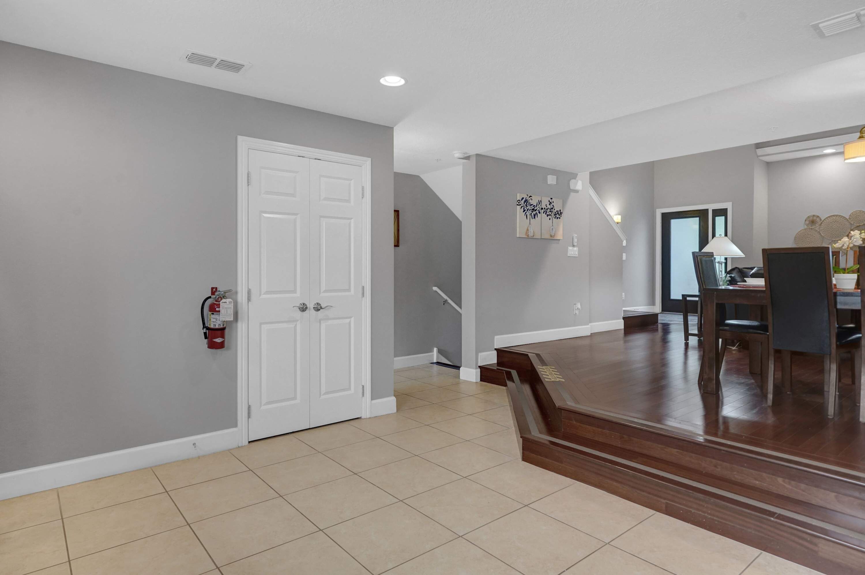 A spacious hallway with a white door, a fire extinguisher, and a staircase leading to another level.