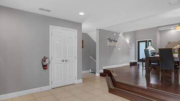 A spacious hallway with a white door, a fire extinguisher, and a staircase leading to another level.