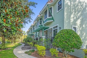 A row of townhouses with a green facade, a curved pathway, and well-maintained landscaping. - Family Townhome Near Disney w Pool Spa Access (Orlando)