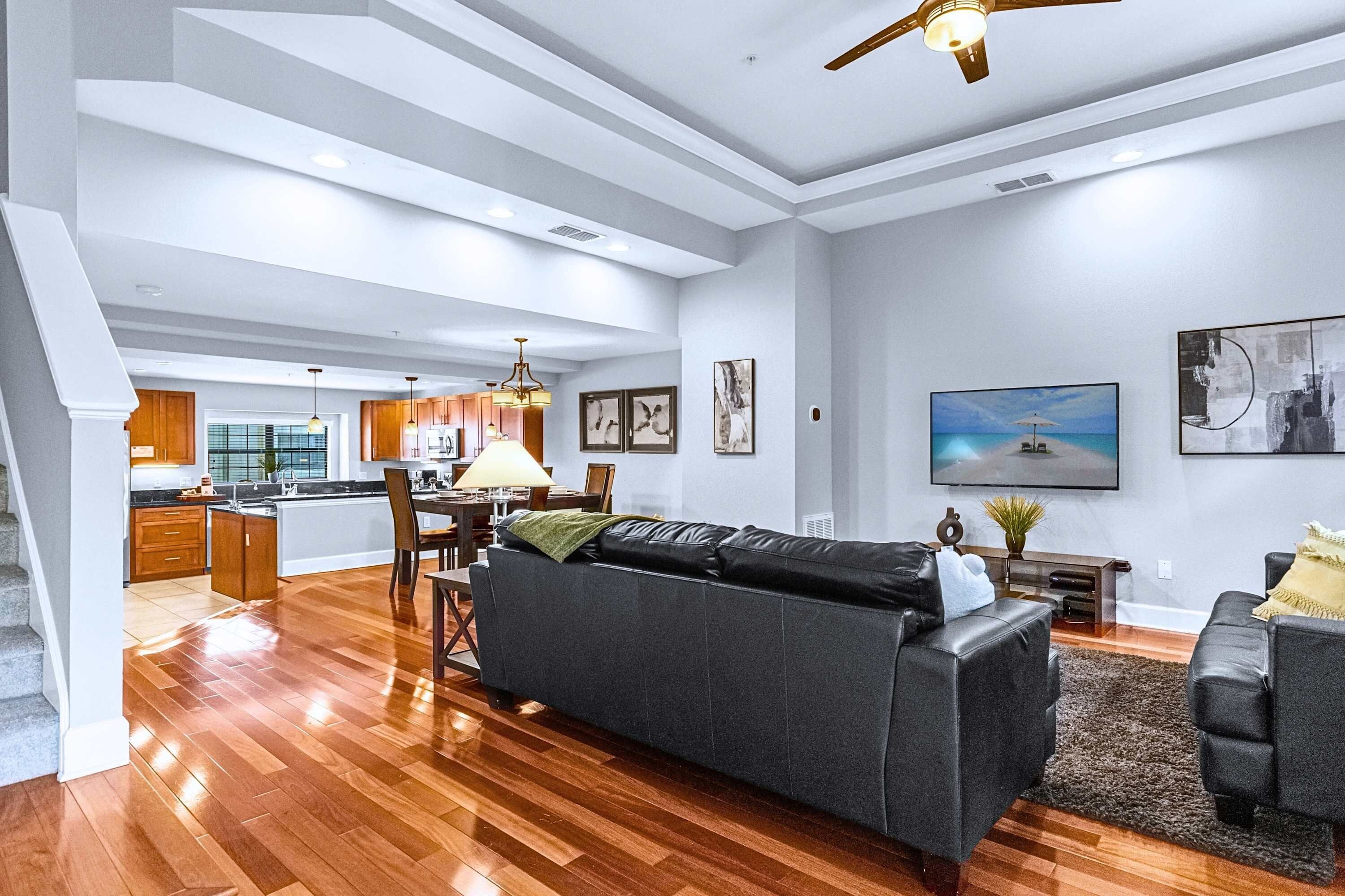 A spacious living area with a dark grey sofa, wooden flooring, and a ceiling fan.