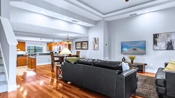 A spacious living area with a dark grey sofa, wooden flooring, and a ceiling fan.