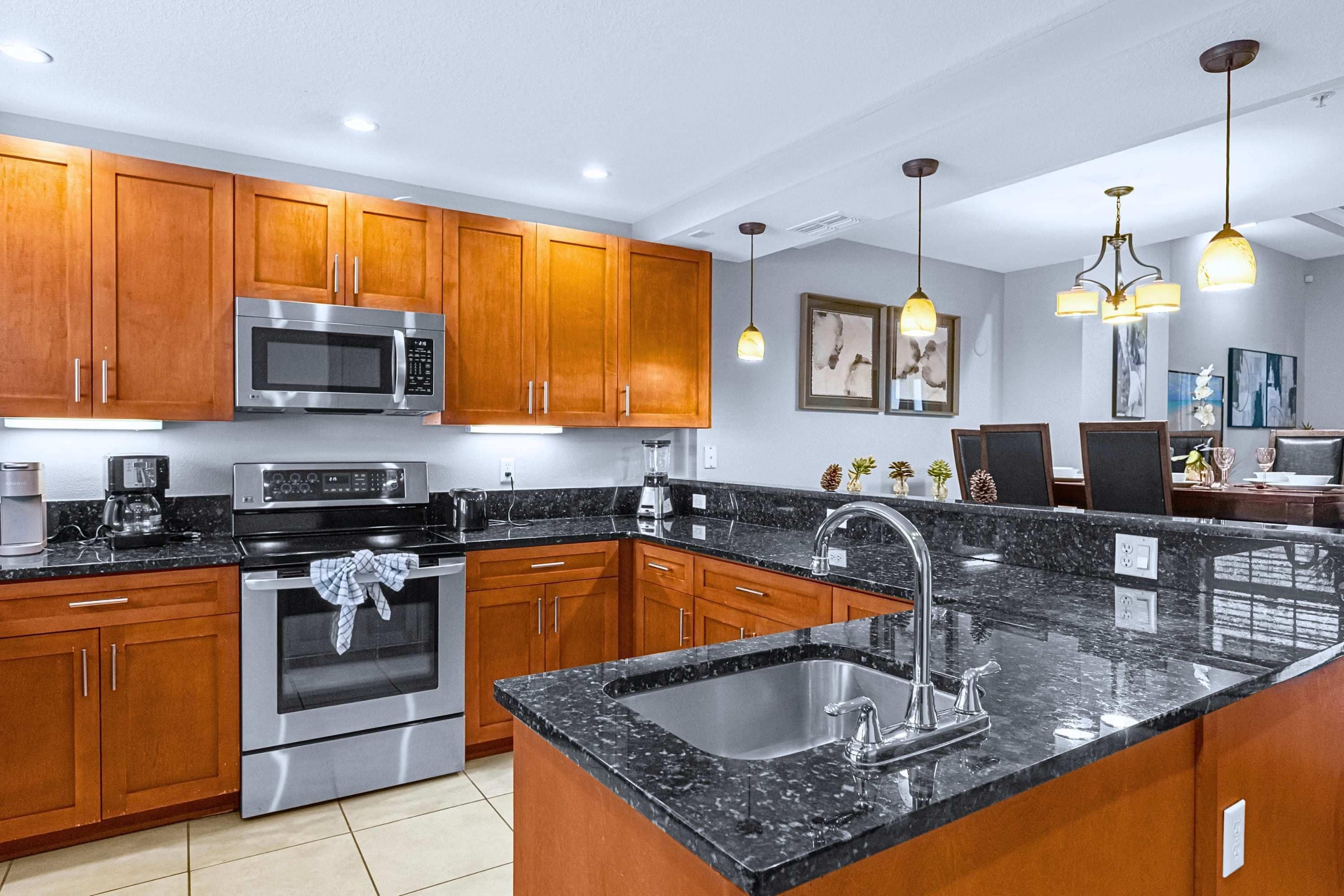 Una cocina moderna con armarios de madera, electrodomésticos de acero inoxidable, encimera de granito e iluminación colgante.