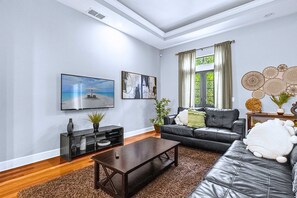 Uma sala de estar moderna com televisão de tela plana, um sofá, uma mesa de centro e uma janela grande com cortinas.
