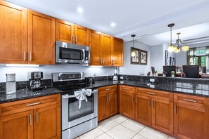 A modern kitchen with wooden cabinets, stainless steel appliances, and a granite countertop. - Family Home Near Disney w Pool Spa Giant Chess (Orlando)