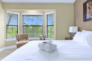 Quarto de hotel com uma cama grande, uma cadeira, uma mesa pequena e uma janela com persianas.