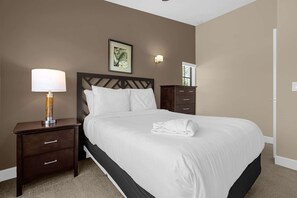 Quarto de hotel com cama, mesa de cabeceira com abajur, luminária na parede e porta.