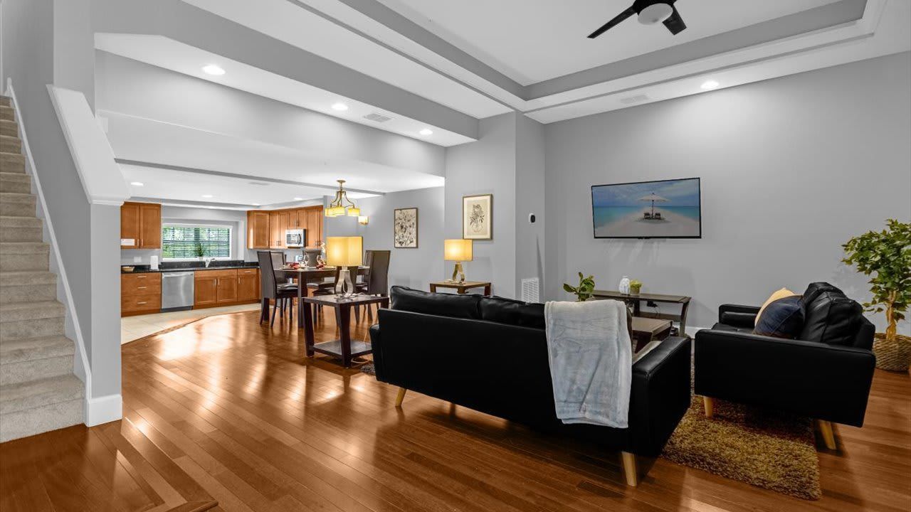A spacious living area with a black sofa, a dining table, and a kitchen in the background.