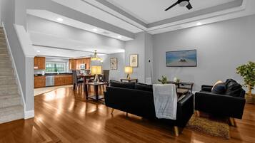 A spacious living area with a black sofa, a dining table, and a kitchen in the background.