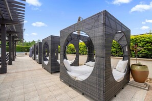 Sitzbereiche im Freien mit Korbmöbeln, weißen Kissen, einer Pergola und einem Blumentopf.