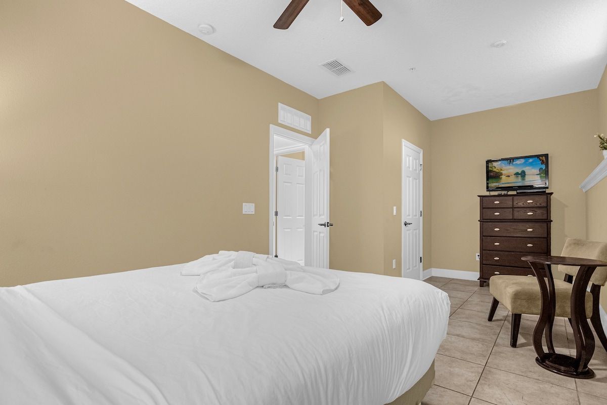 A bedroom with a large bed, a dresser, a television, and a chair.