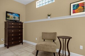 A room with a television on a dresser, a chair, a small table, a plant on a shelf, and a window with a view. - Home Near Disney With Resort Pool Spa Access (Orlando)