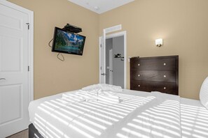 A hotel room with a bed, a television mounted on the wall, a dresser, and a door leading to another room. - Home Near Disney With Resort Pool Spa Access (Orlando)