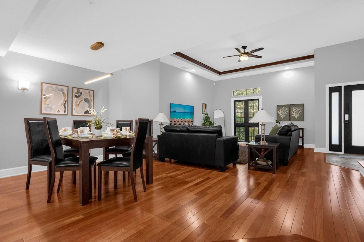 Uma sala de estar ampla com uma mesa de jantar, cadeiras, um sofá e um ventilador de teto.