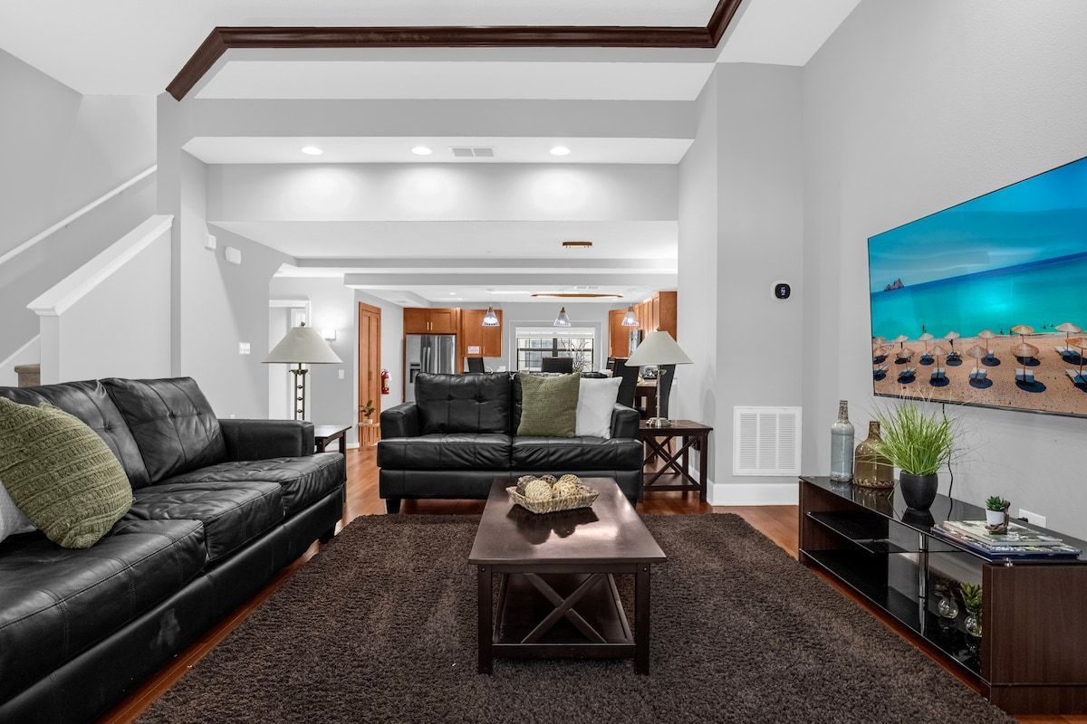 Uma sala de estar moderna com um sofá de couro preto, uma mesa de centro escura e uma pintura grande com uma praia.