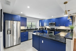 A modern kitchen with blue cabinets, stainless steel appliances, and a granite countertop. - Magical Townhome Near Disney w Resort Pool Access (Orlando)