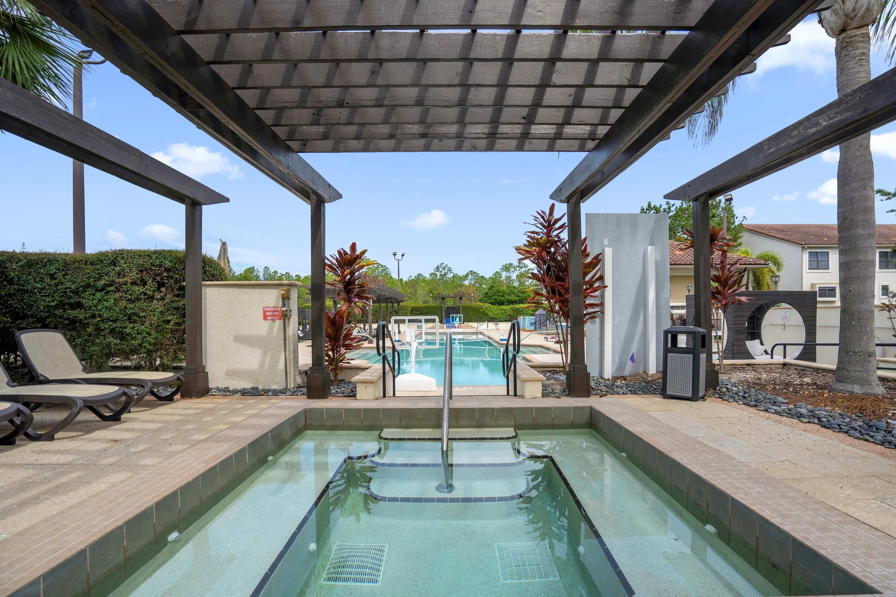 Área de piscina com hidromassagem, espreguiçadeiras e um espaço de estar coberto.