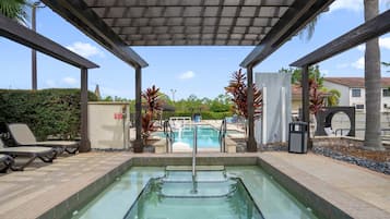 Área de piscina com hidromassagem, espreguiçadeiras e um espaço de estar coberto.