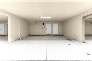 Ein leerer Raum mit weißen Wänden, einer weißen Decke und einem Betonboden. Es gibt zwei weiße Türen und eine Leuchte an der Wand.