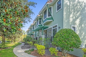 A row of townhouses with a green facade, a stone pathway, and well-maintained landscaping. - Family Vacation Home Near Disney w Pool Spa (Orlando)