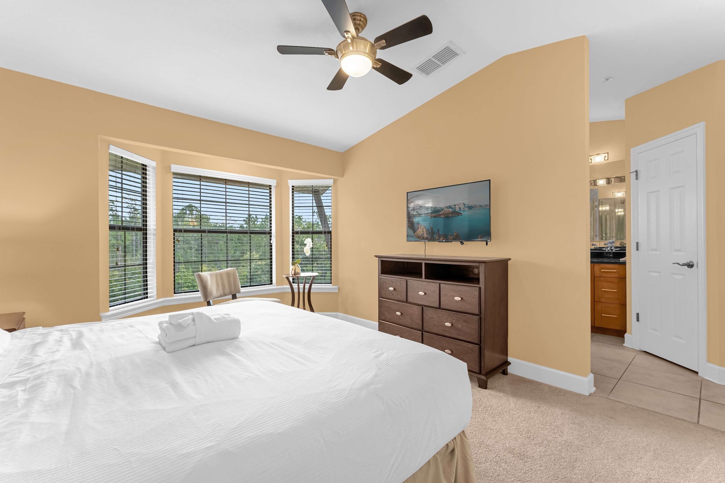 A bedroom with a bed, a dresser, a ceiling fan, and a window with blinds.