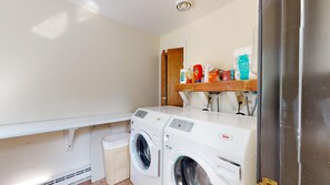 A laundry area with two front-loading washing machines, a small trash bin, and a shelf with various cleaning supplies. - 2BR condo w/ fireplace, ski locker, pool, sauna, tennis (Waitsfield)