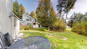 A residential property with a fenced yard, a metal table, and a building with a green roof. - 2BR condo w/ fireplace, ski locker, pool, sauna, tennis (Waitsfield)