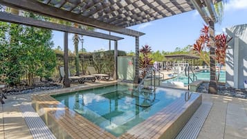 A pool area with a pergola, lounge chairs, and a view of a second pool.