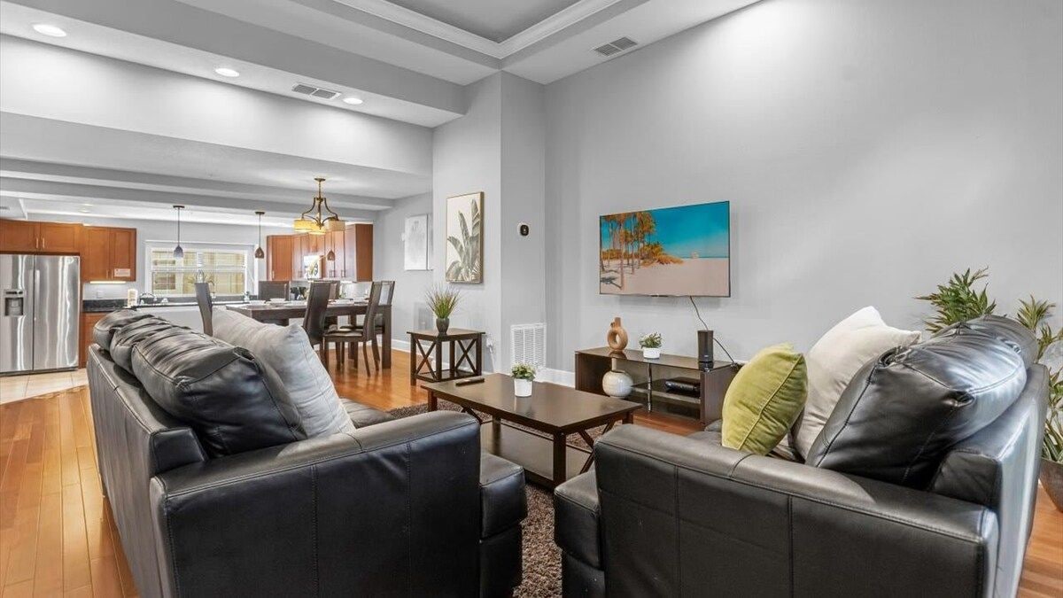Uma sala de estar moderna com conjunto de sofá, área de jantar e cozinha ao fundo.
