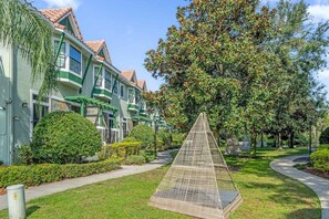 Un edificio residencial con fachada verde y blanca, un elemento de jardín triangular y un camino que lleva a la entrada.