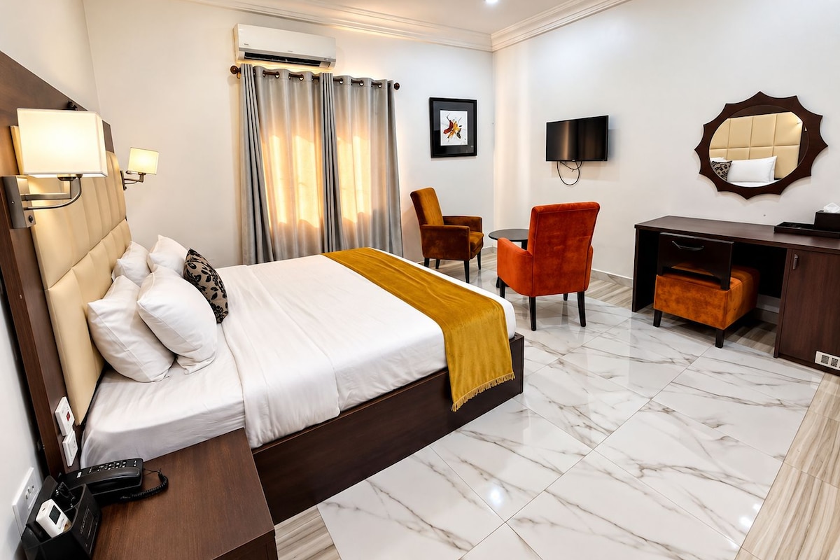Een hotelkamer met een bed, een bureau, een stoel, een televisie en een airconditioning.
