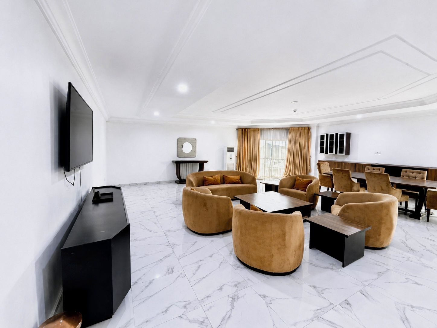Una habitación de hotel moderna con televisión de pantalla plana, un conjunto de sofás, una mesa de comedor y un amplio ventanal con cortinas.