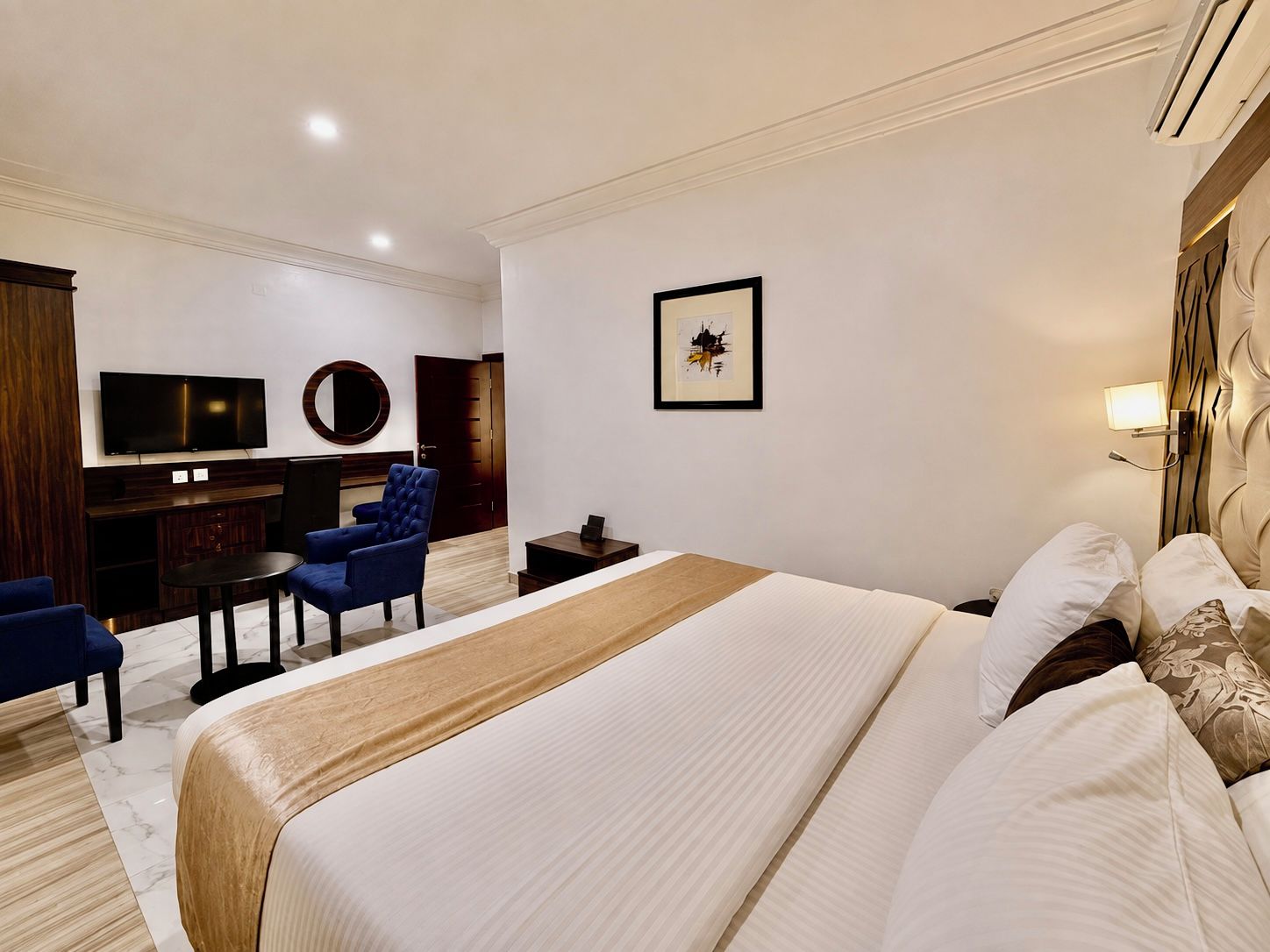Habitación de hotel con una cama grande, un escritorio con silla, un televisor y un cuadro en la pared.