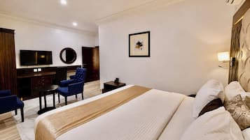 Habitación de hotel con una cama grande, un escritorio con silla, un televisor y un cuadro en la pared.
