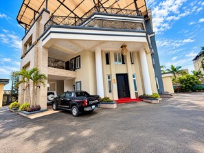 A multi-story building with a black pickup truck parked in front, a red carpet leading to the entrance, and a balcony with wrought iron railings.